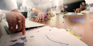 business documents on office table with smart phone and laptop computer and graph business with social network diagram and two colleagues discussing data in the background